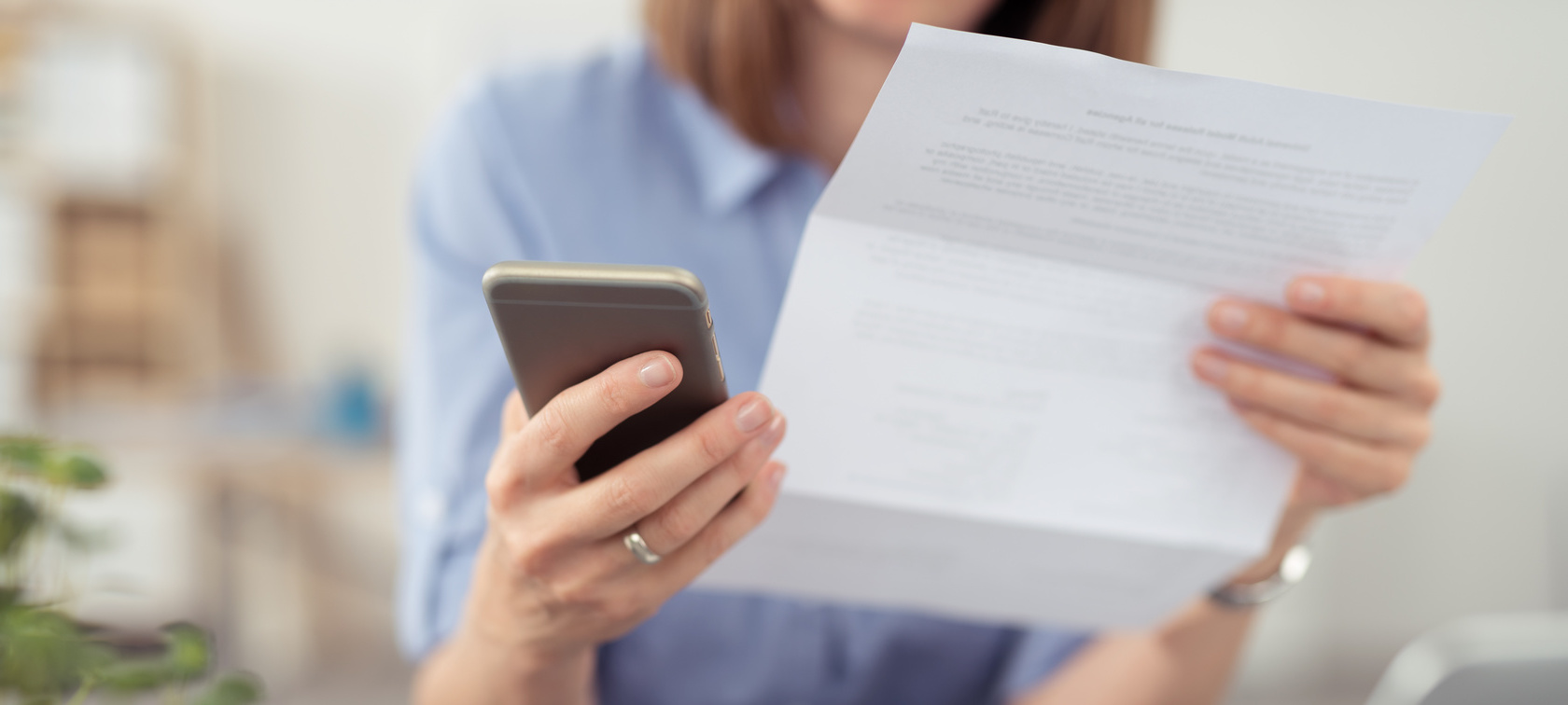 Frau hält Telefon in der Hand und liest eine Rechnung Frau hält Telefon in der Hand und liest eine Rechnung